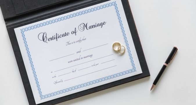 Photograph of a marriage certificate with wedding rings on