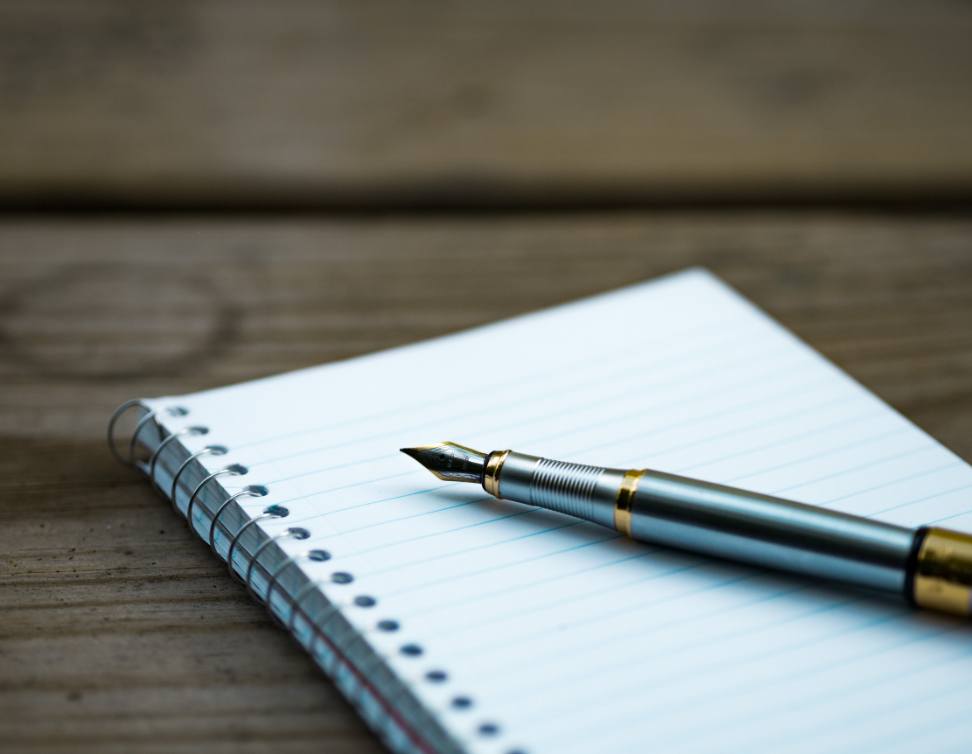 Photo of a pad of paper on a table, with a pen resting on top