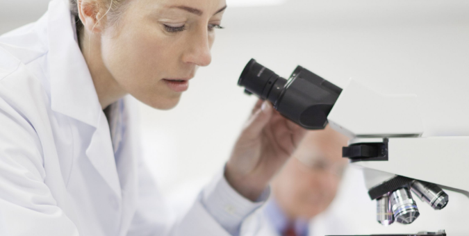 Widescreen image of a coroner looking at something through a microscope