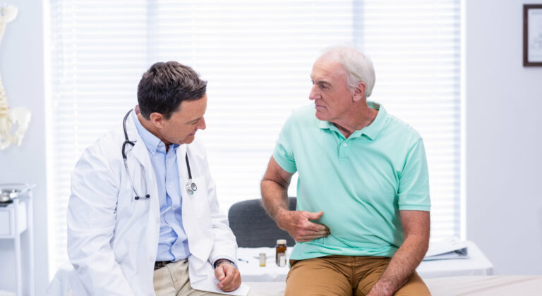 A man holds his stomach while talking to a doctor