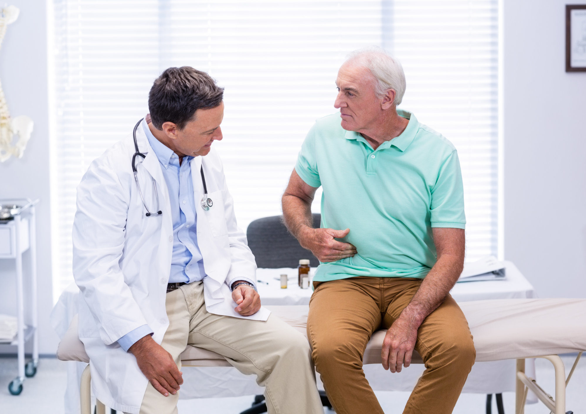 A man holds his stomach while talking to a doctor