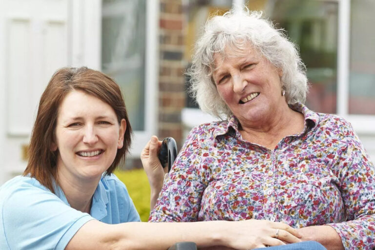 A carer smiles with an older lady in a wheelchair