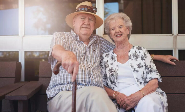 An elderly couple sit together outside
