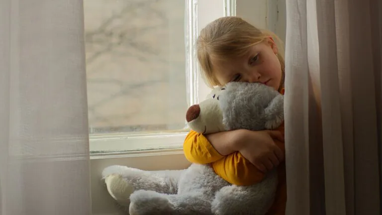 Sad,Little,Girl,Child,Sitting,Looking,At,Window,Hugging,Teddy
