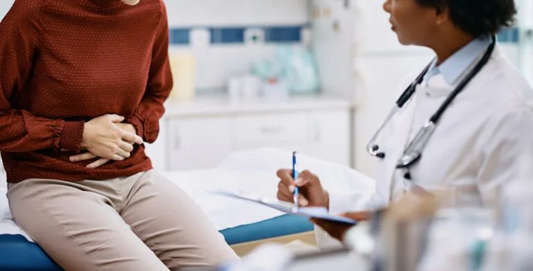 Female,Patient,Holding,Her,Abdomen,In,Pain,While,Talking,To