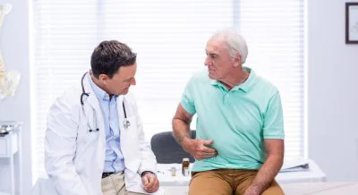 A man holds his stomach while talking to a doctor