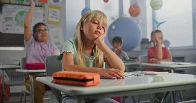 Sad,Primary,School,Girl,Sitting,At,Desk,,Getting,Tired,During